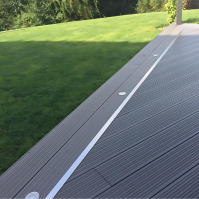 Terrasse en composite gris anthracite avec finition en aluminium, spots encastrés et pelouse verdoyante.
