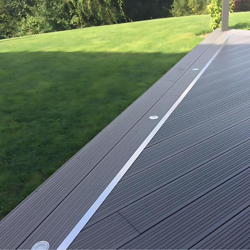 Terrasse en composite gris anthracite avec finition en aluminium, spots encastrés et pelouse verdoyante.