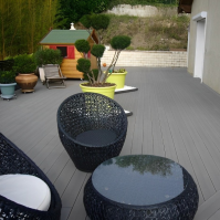 Terrasse moderne en composite gris anthracite, avec salon de jardin et pot de fleurs Fuji, alliant confort et esthétique.